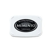 Weißes Stempelkissenetui mit der Aufschrift Tsukineko Memento Tuxedo Black mit schwarzem ovalen Logo und weißem Text, mit schnell trocknender Tinte für gestochen scharfe Abdrücke. Ideal für die Verwendung mit Memento Stempelfarbe.