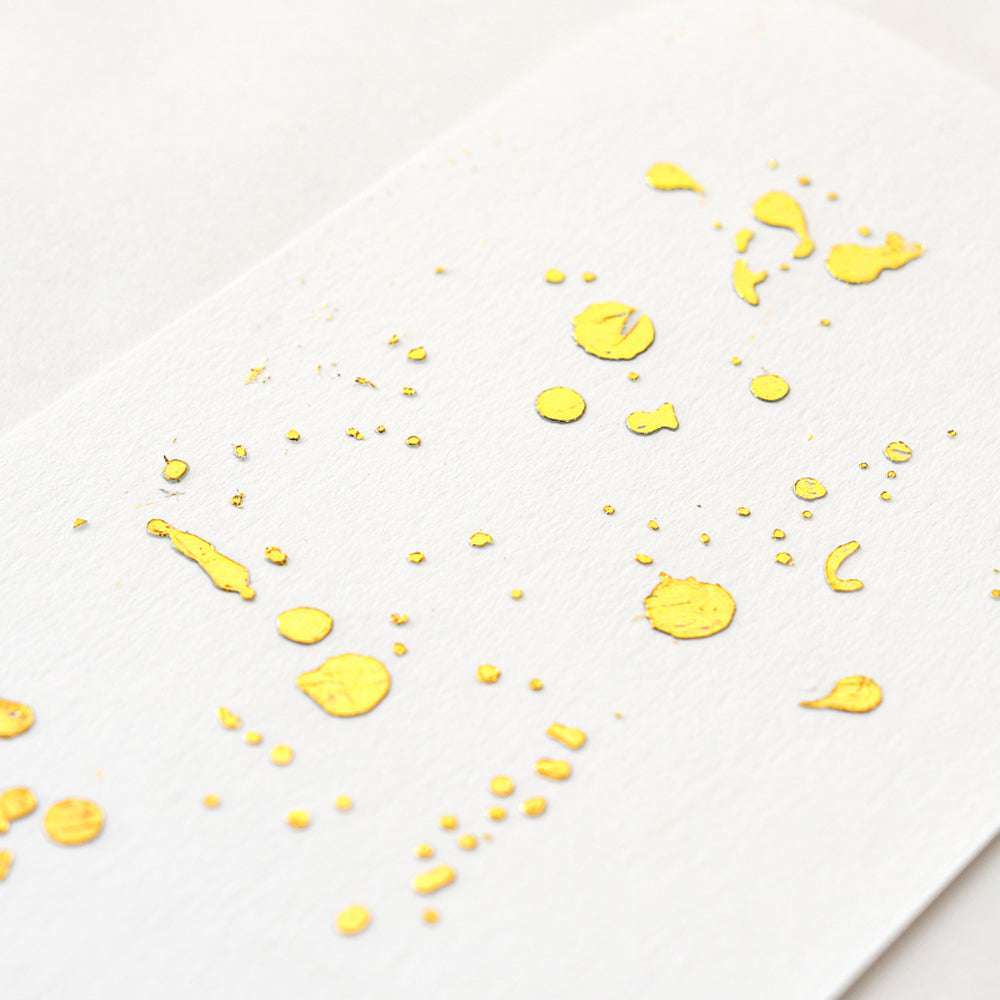 Gelbe Farbspritzer auf weißem Strukturpapier, mit Punkten und Klecksen, sorgen für einen verspielten Look - ideal zur Kombination mit ☆ Heißfolie Gold, um Ihren kreativen Projekten ein edles Finish zu verleihen.
