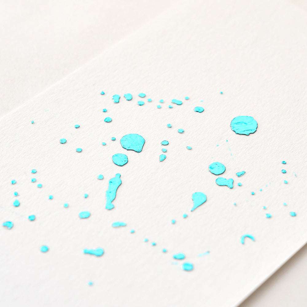 Leuchtend blaue Farbspritzer auf weißem Strukturpapier bilden ein edles Finish - ideal zur Kombination mit ☆ Heißfolie Aqua, um Ihre kreativen Projekte aufzuwerten.