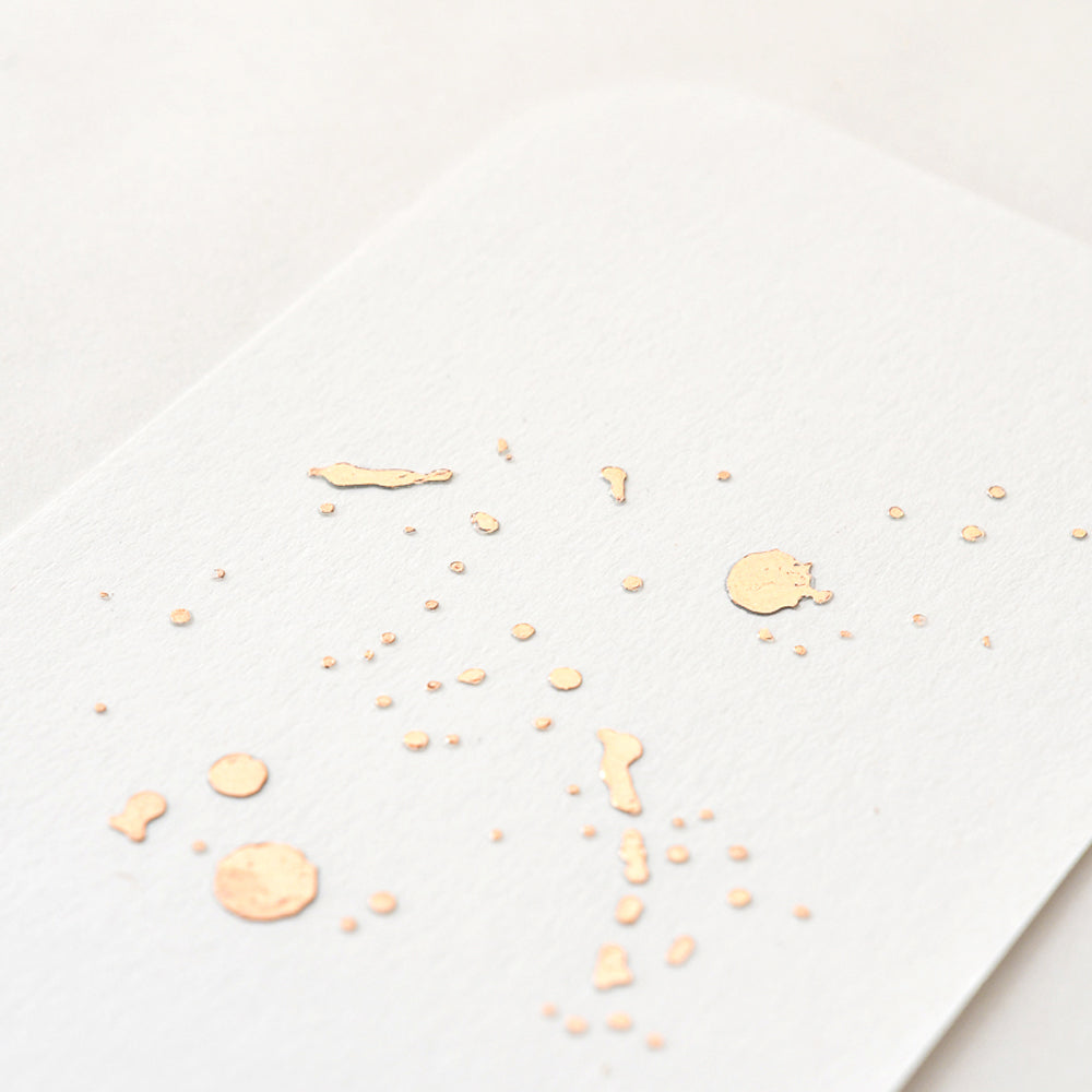 Strukturiertes weißes Papier mit kleinen roségoldenen Folienspritzern und abgerundeten Kanten von ☆, ideal für Bastelprojekte. Vor einem sauberen weißen Hintergrund.