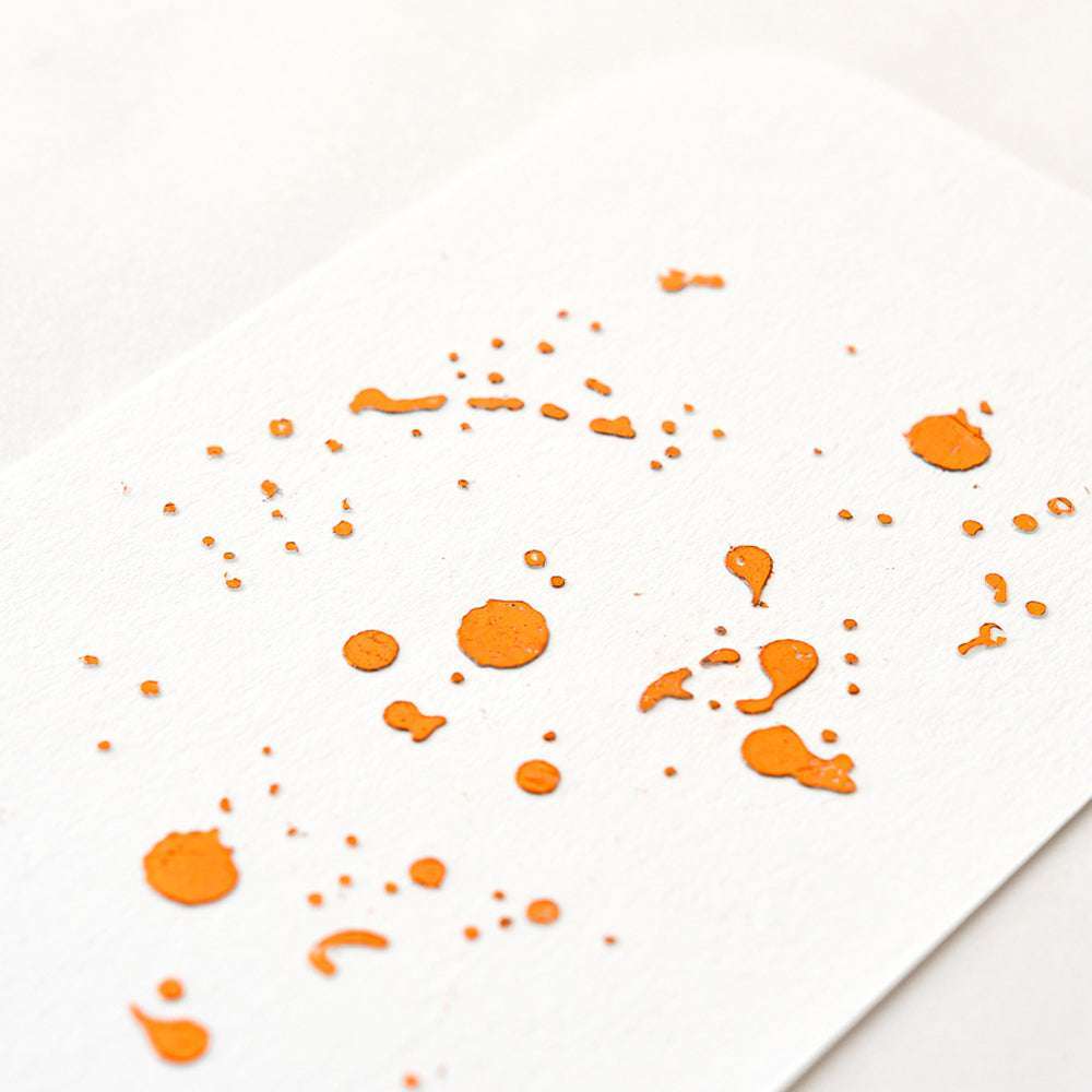 Orangefarbene Farbspritzer auf weißem Strukturpapier, die den leuchtenden Glanz der ☆ Heißfolie Orange für kreative Projekte hervorrufen.