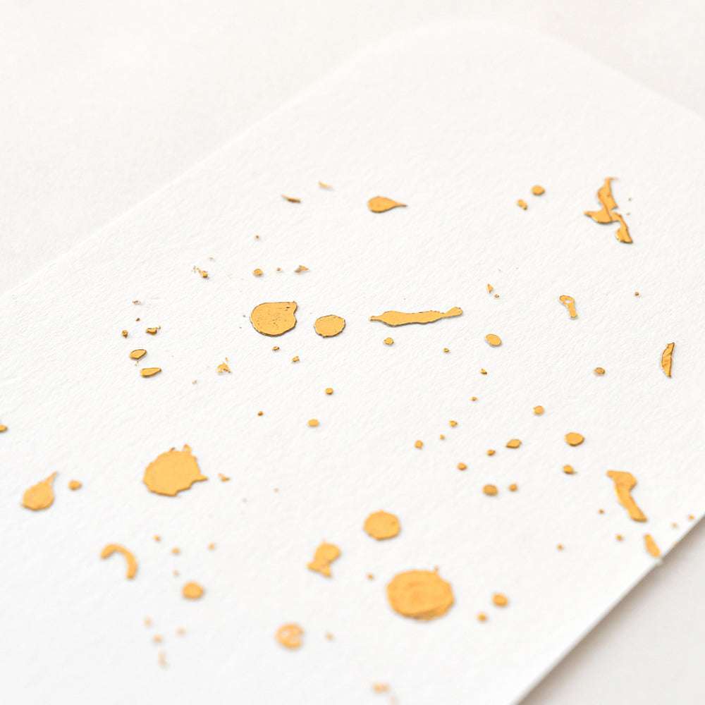 Weißes Papier mit vereinzelten goldenen Farbspritzern, schräg betrachtet, strahlt Eleganz Exklusivität aus. Der Effekt ähnelt dem von ☆ Tacky-when-Dry Paste in Kombination mit Heißfolie Orangegold matten Akzenten.