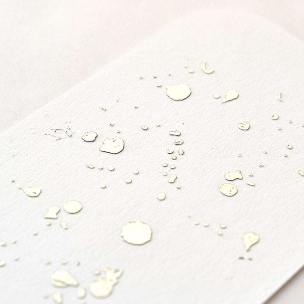 Weißes Strukturpapier mit verstreuten goldenen Metallic-Tintenspritzern und Punkten von ☆-ideal für Heißfolien-Transfer oder das Hinzufügen von Bastelfolie-Akzenten zu Ihren kreativen Projekten.