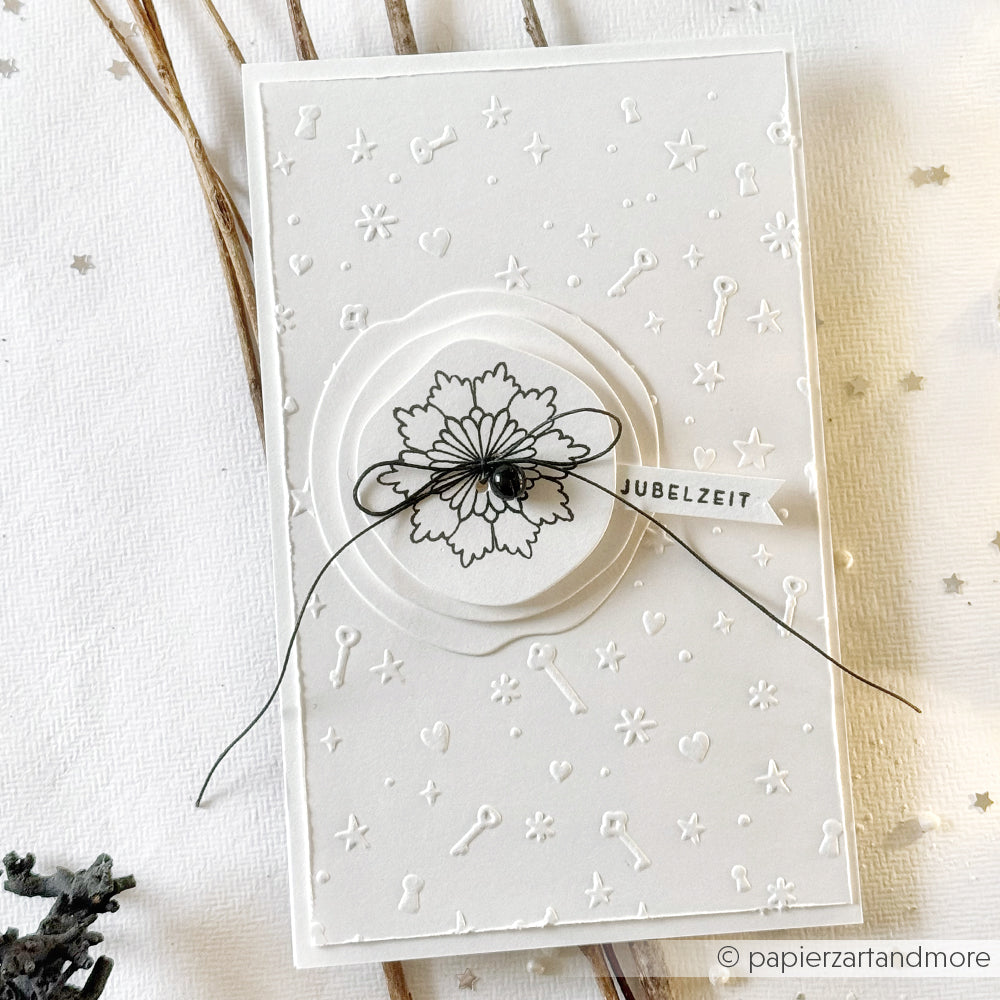 Weiße Prägekarte von Alexandra Renke mit schwarzem Blumenmuster, schwarzem Faden und einem JUBELZEIT-Anhänger - hergestellt mit einem Cut & Emboss Folder für mehr Struktur und Eleganz.