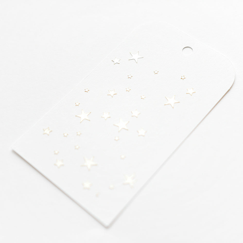 Weißer Anhänger von Alexandra Renke mit kleinen, glänzend geprägten Sternen in einer Schablone Sterne Muster mit oberem Loch, auf weißem Hintergrund - ideal für Papierprojekte oder zur Kombination mit Schablonen.