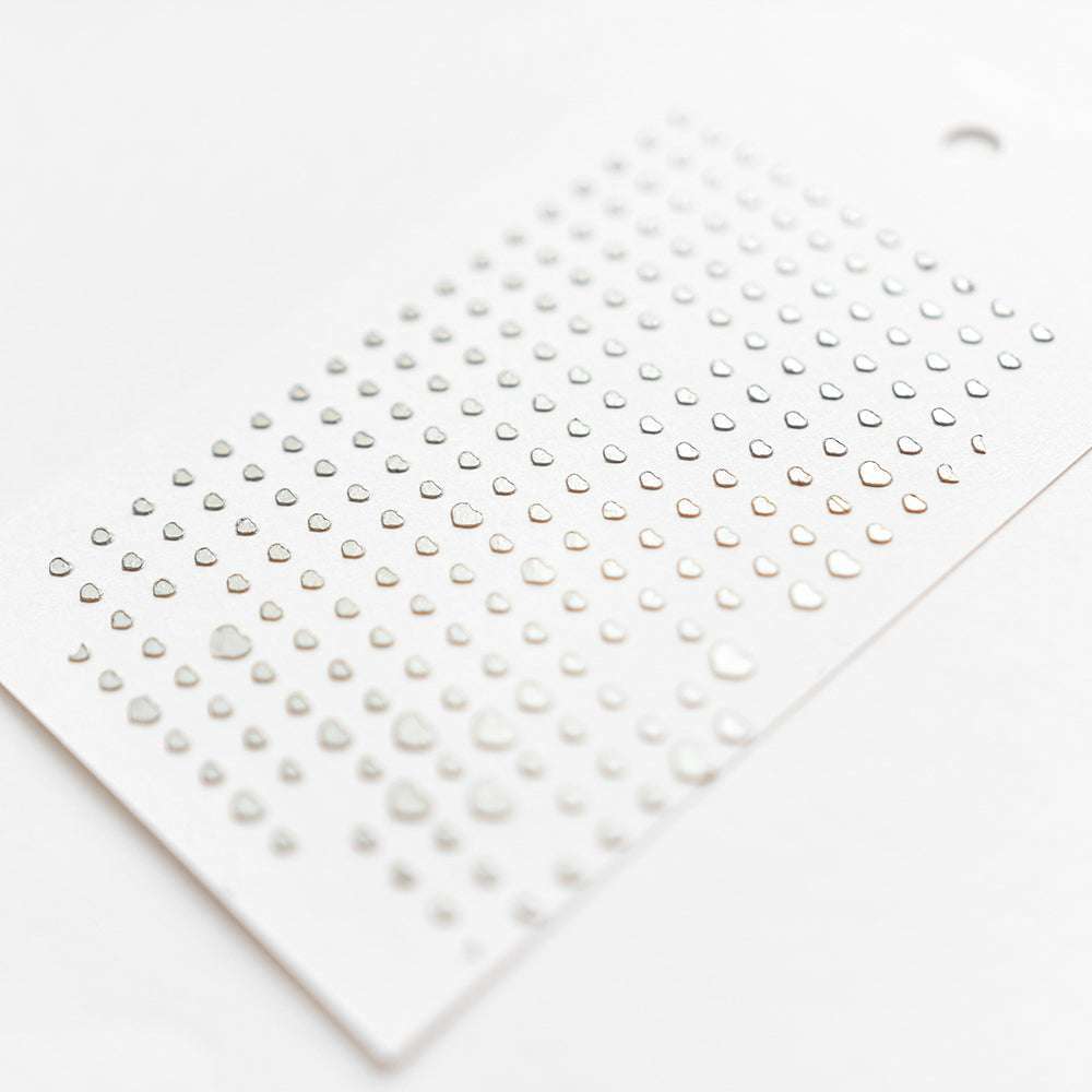 Ein Bogen mit kleinen metallisch-silbernen Herz-Stickern von Alexandra Renke, fein säuberlich angeordnet auf weißem Papier - ideal für Papierprojekte oder als Stencil Herz-Raster für kreative Bastelarbeiten.