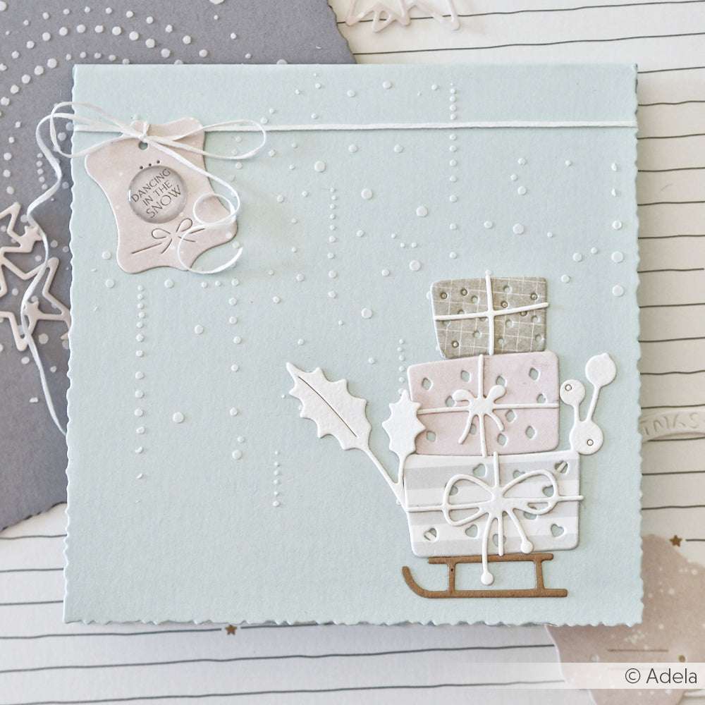 Hellblaue Weihnachtskarte von Alexandra Renke mit gestapelten Geschenken auf einem Schlitten, weißer Schnur und einem Geschenkanhänger mit Schneemotiv - ideal für Papierprojekte oder zum Verzieren mit Schablonen und Stencil Sektperlen.