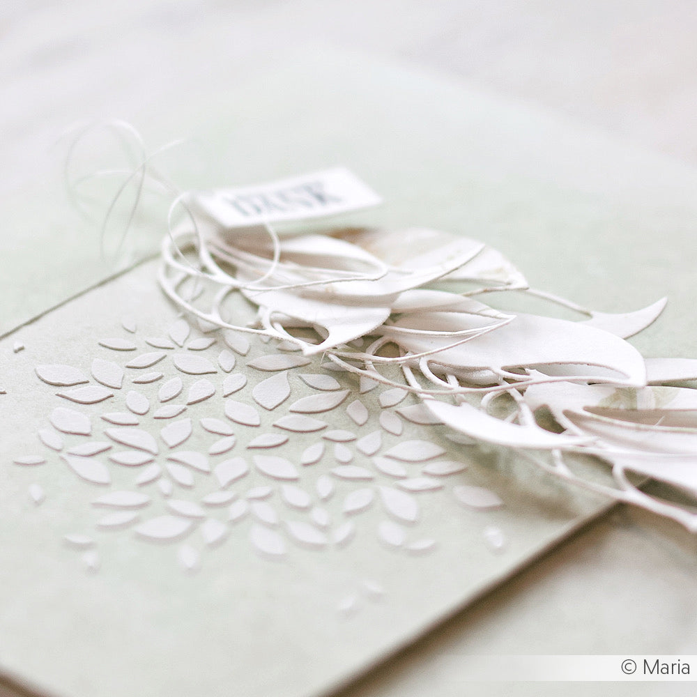 Eine strukturierte Karte mit zarten weißen Papierblättern und filigranen Ausschneidemustern auf hellem Hintergrund, die mit Alexandra Renkes Schablone Papierprojekte für elegante, wiederverwendbare Blattformen hergestellt wurde.