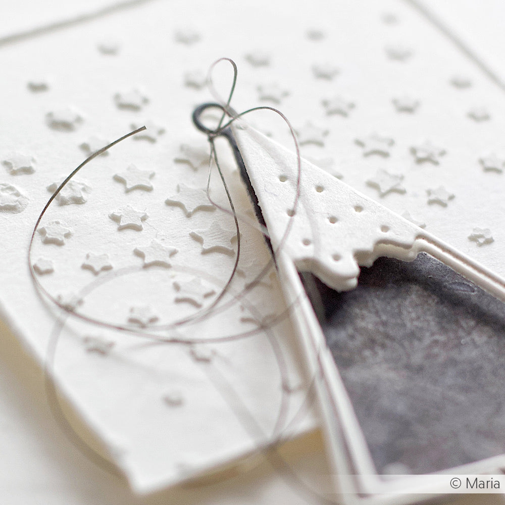 Nahaufnahme einer weißen, strukturierten Karte von Alexandra Renke mit Stencil Sterne und einer Nadel, die eine schwarze Schnur durch ein Papierdreieck zieht - ideal für kreative Schablonen- und Papierprojekte.