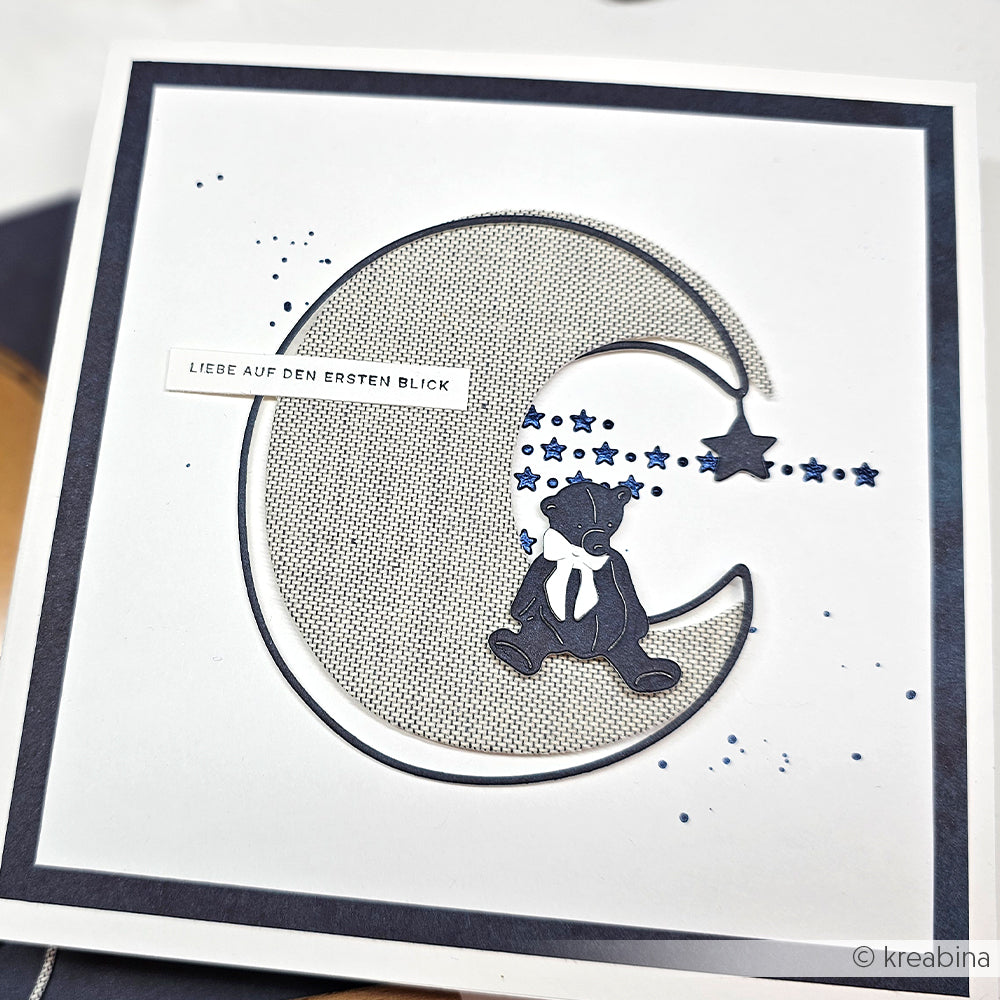 Handgemachte Karte von Alexandra Renke mit einem Bären im Schal auf einem Mond mit blauen Sternen (Schablone Papierprojekte); Text: LIEBE AUF DEN ERSTEN BLICK.