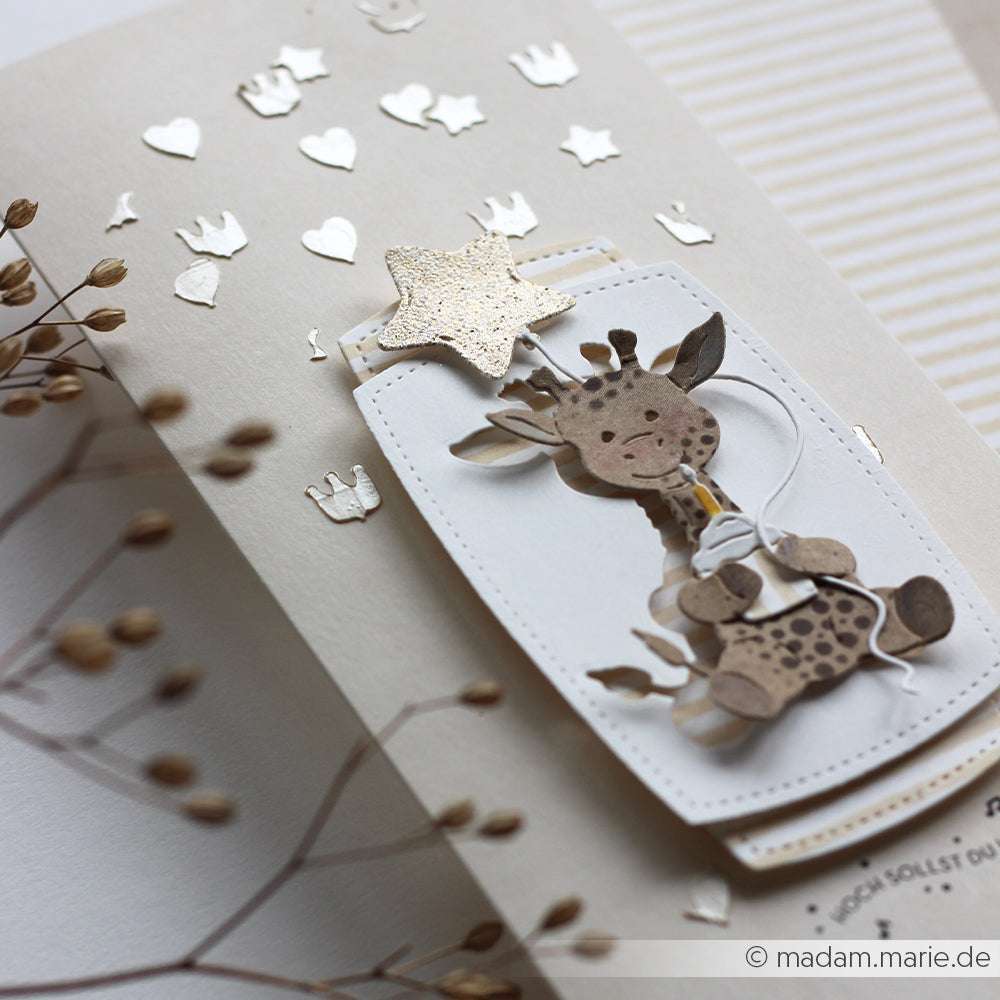 Handgemachte Karte mit einer niedlichen Giraffe, einer weißen Schleife, einem goldenen Stern und Metallic-Herzen im Hintergrund, hergestellt mit der Schablone Ballonfreunde Schablonen von Alexandra Renke.