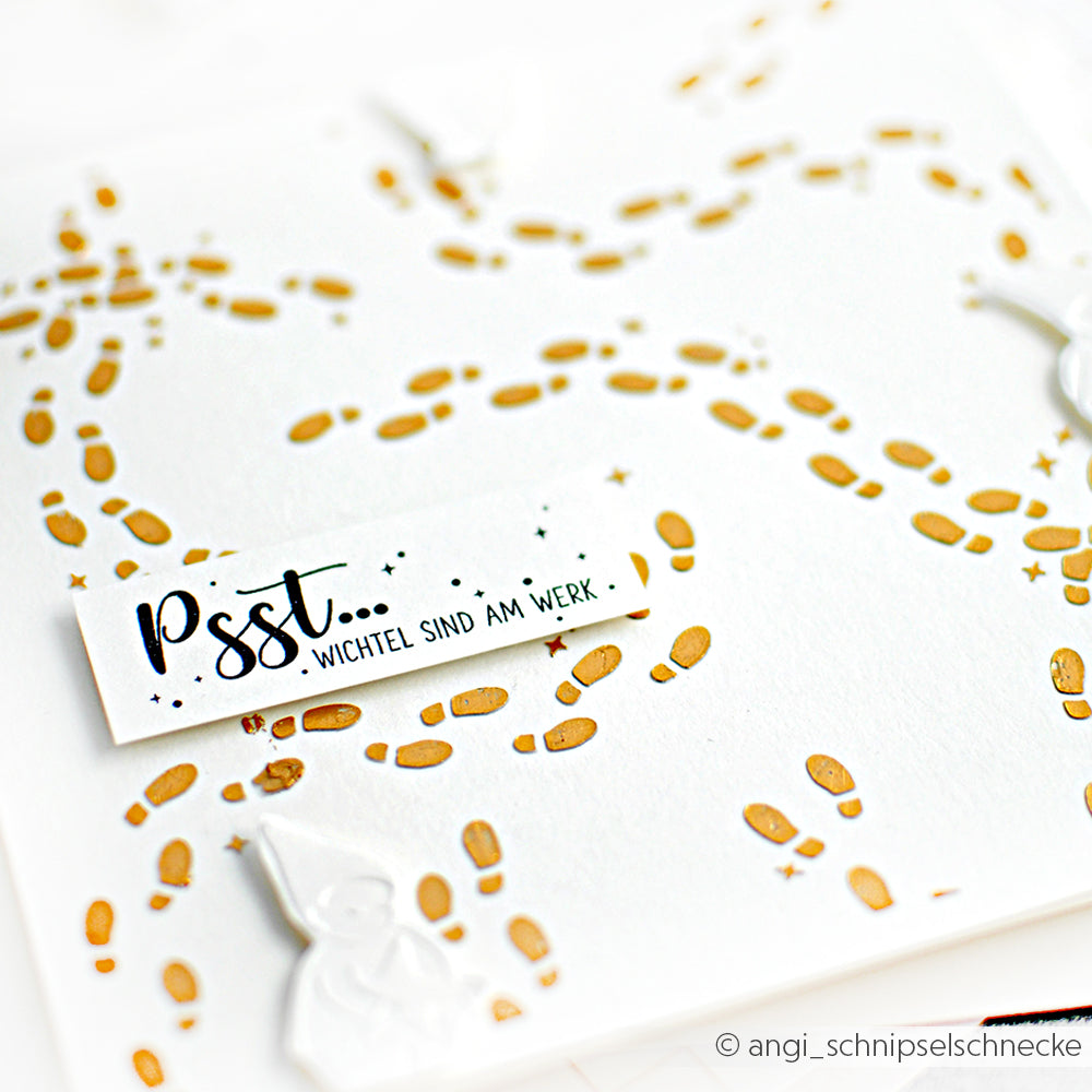 Weißes Papier von Alexandra Renke mit verstreuten goldenen Wichtelspuren, die mit einer Schablone erstellt wurden, und der Aufschrift "Psst... Wichtel sind am Werk.