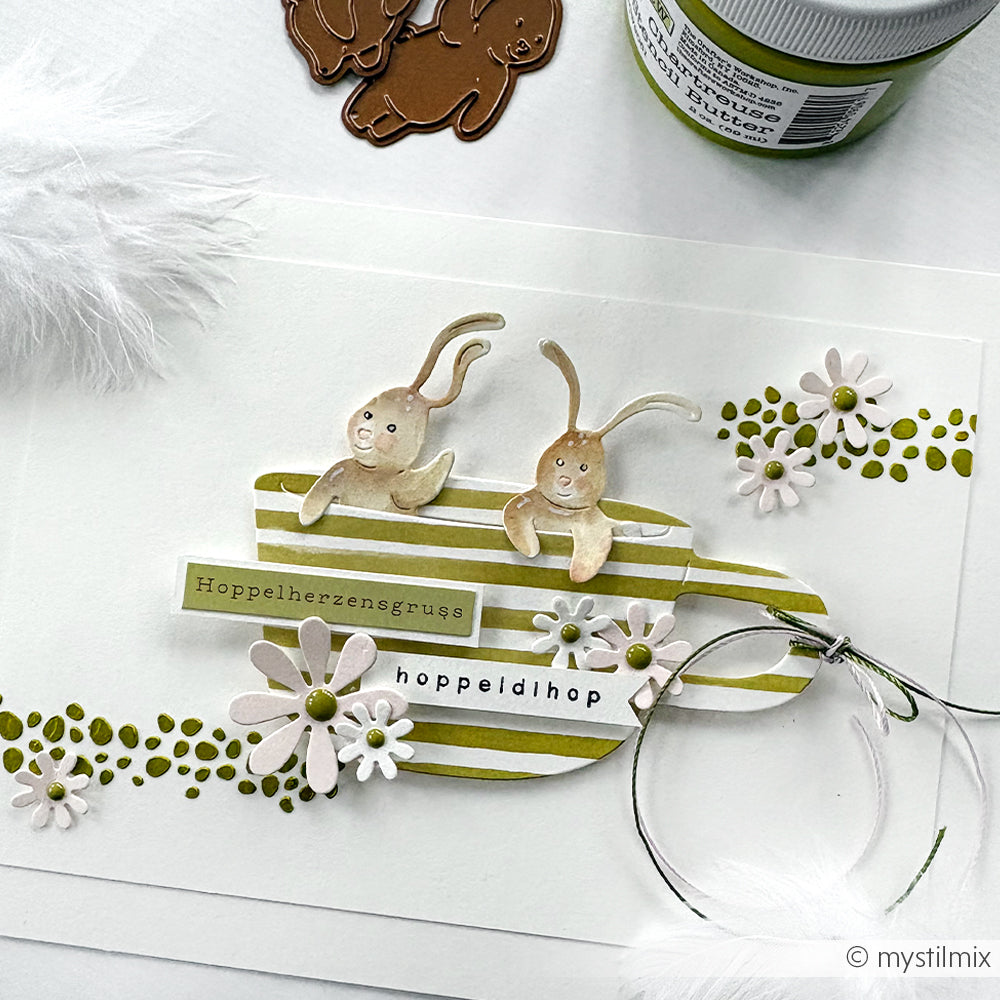 Handgefertigte Alexandra Renke Karte mit zwei Hasen, Blumen und deutschem Text in grün, weiß und braun. Gefertigt mit wiederverwendbaren Schablonen und Stencil Eierformen für einzigartige dekorative Elemente.