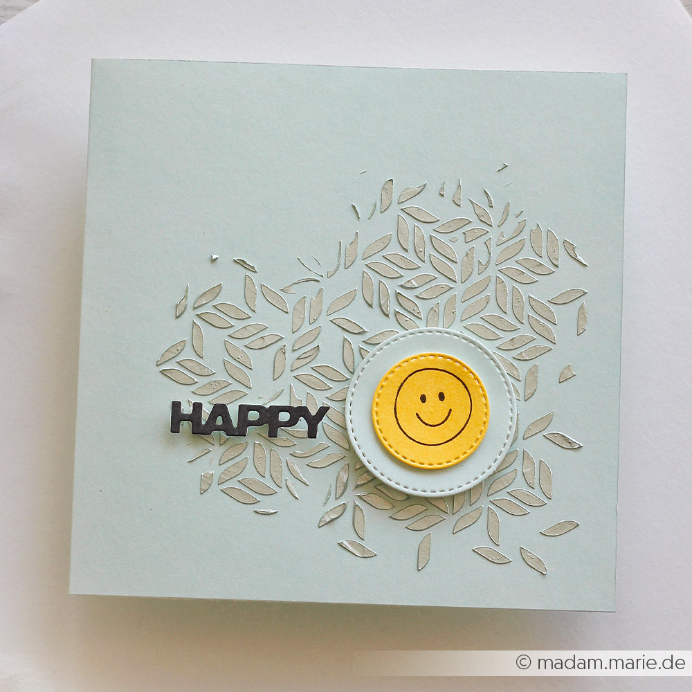 Quadratische Karte mit dem Schriftzug „HAPPY“, einem Smiley und einem zarten Blatt-Ausschnittmuster im Hintergrund – perfekt für Schablonen-Papierprojekte oder alle, die Inspiration für geometrische Schablonendesigns suchen.