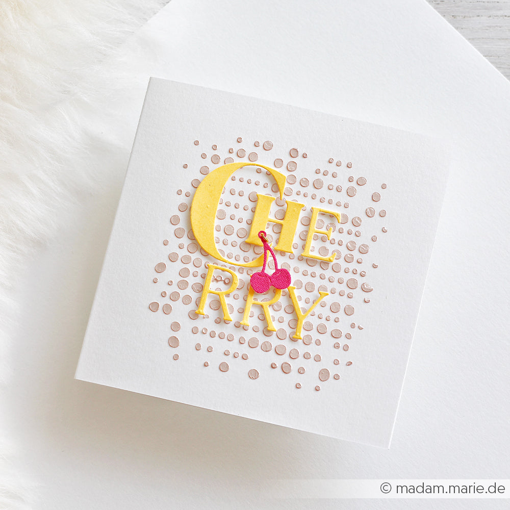 Quadratische Karte mit der Aufschrift „CHERRY“ in gelben Buchstaben und zwei rosa Kirschen auf einem gepunkteten beigen Hintergrund, inspiriert vom Stencil-Punktemuster – perfekt für Schablonen-Papierprojekte und kreative Anwendungen mit wiederverwendbaren Schablonen.