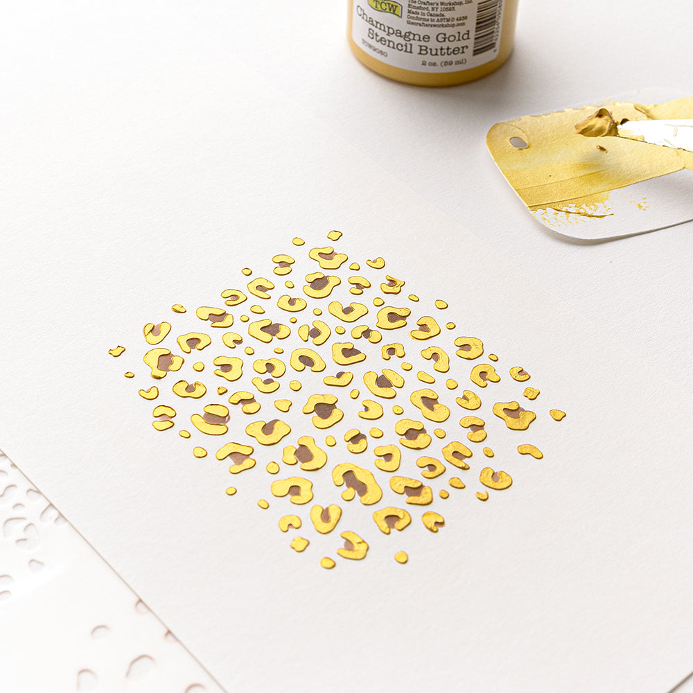Ein gold-braunes Leopardenmuster auf weißem Papier, erstellt mit der Schablone „Geschichteter Leopardenprint“ und wiederverwendbaren Schablonen, mit Goldpaste und einem Spachtel daneben.