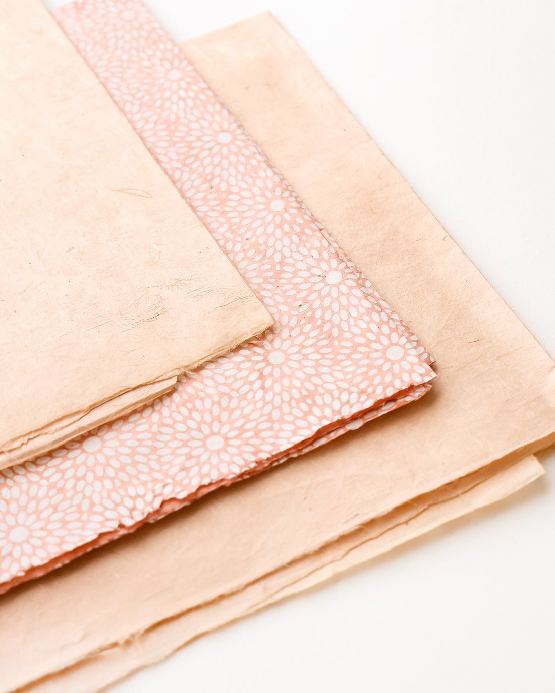 Drei Blätter Dekorationspapier, eines davon mit einem rosafarbenen Blumenmuster, gestapelt auf einer weißen Fläche.