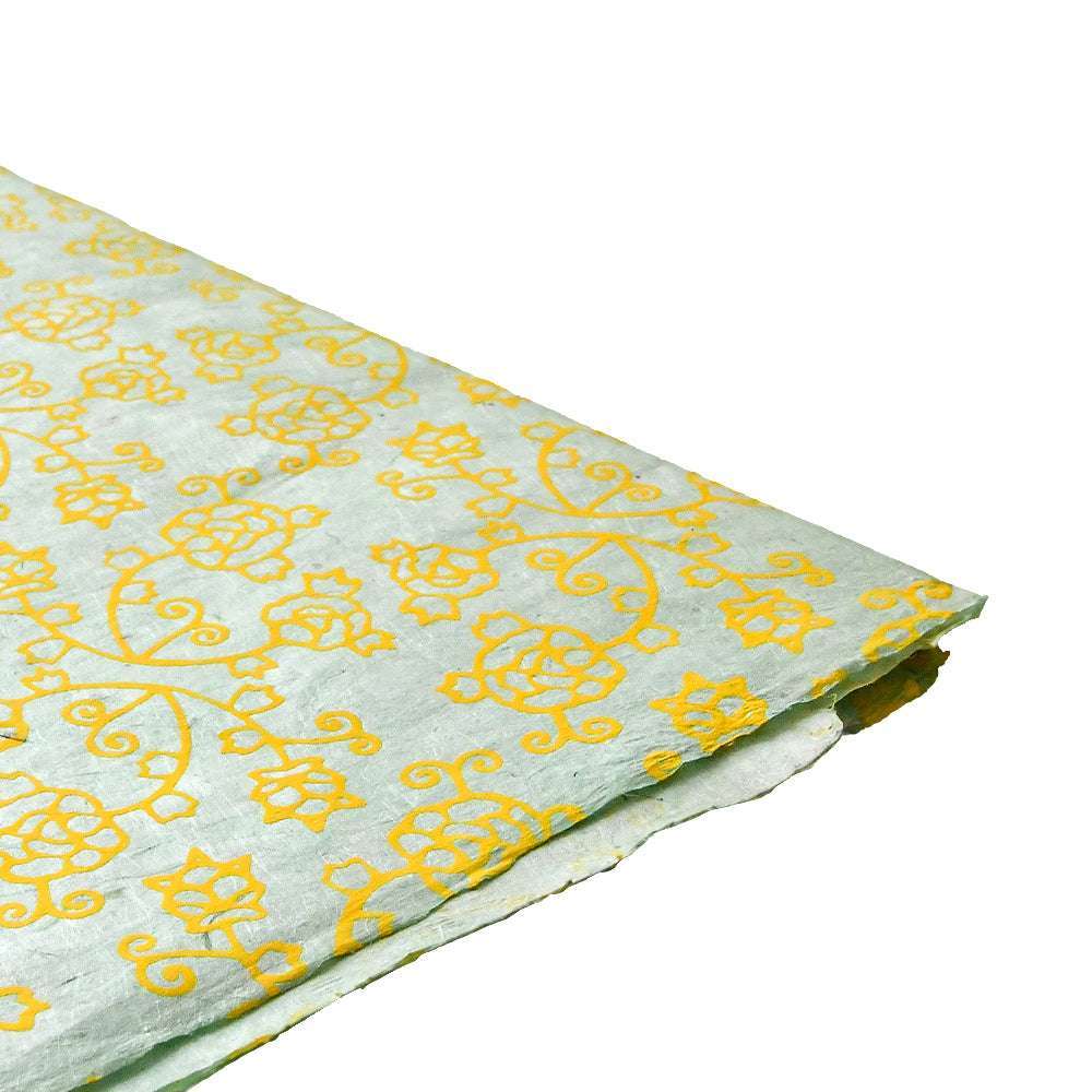 Blatt hellblaues Nepalpapier von ☆ mit gelbem Blumen- und Rankenmuster, an der Ecke teilweise gefaltet - ideal für Geschenkverpackungen oder Buchbindearbeiten.