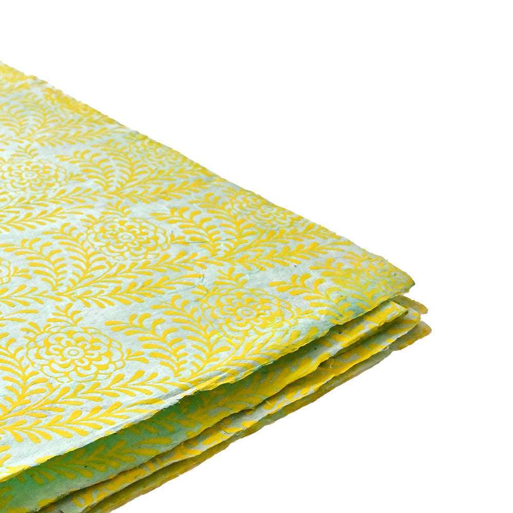 Das gefaltete Nepalpapier zeigt ein gelbes Blumenmuster auf hellblauem Hintergrund, das sich ideal zum Einbinden von Büchern oder zum Verpacken von Geschenken eignet und auf einer weißen Fläche präsentiert wird.