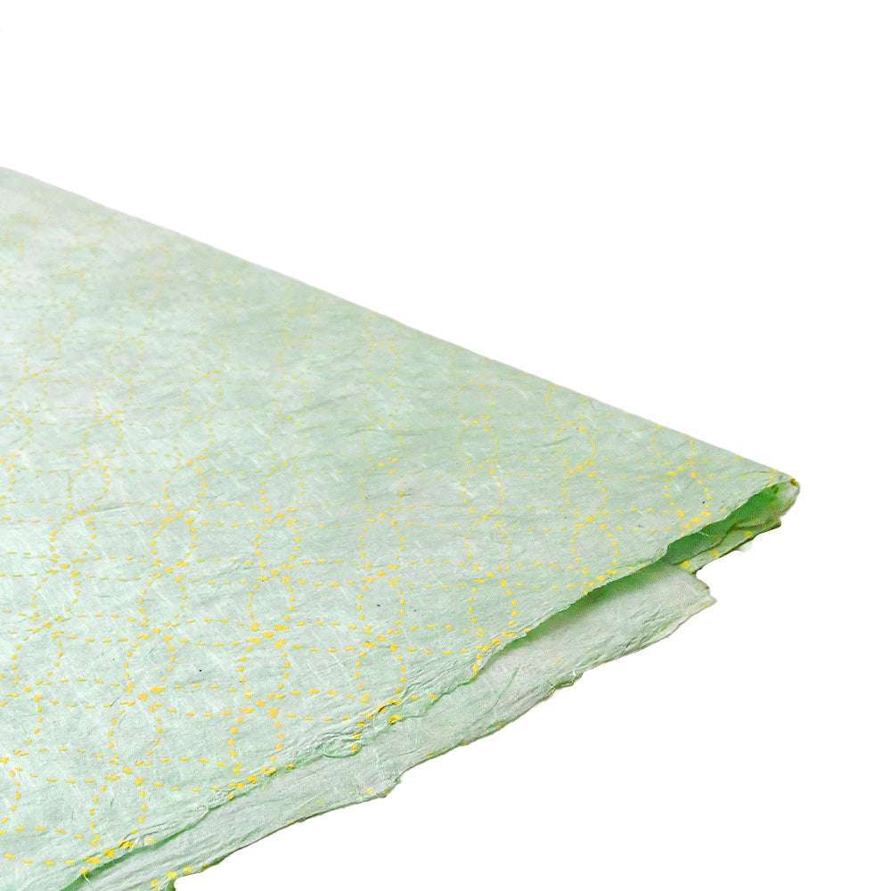 Ein gefalteter Bogen hellgrünen Nepalpapiers von ☆ mit einem dezenten gelben, von Mandalas inspirierten geometrischen Muster - perfekt für Geschenkverpackungen - auf weißem Hintergrund.