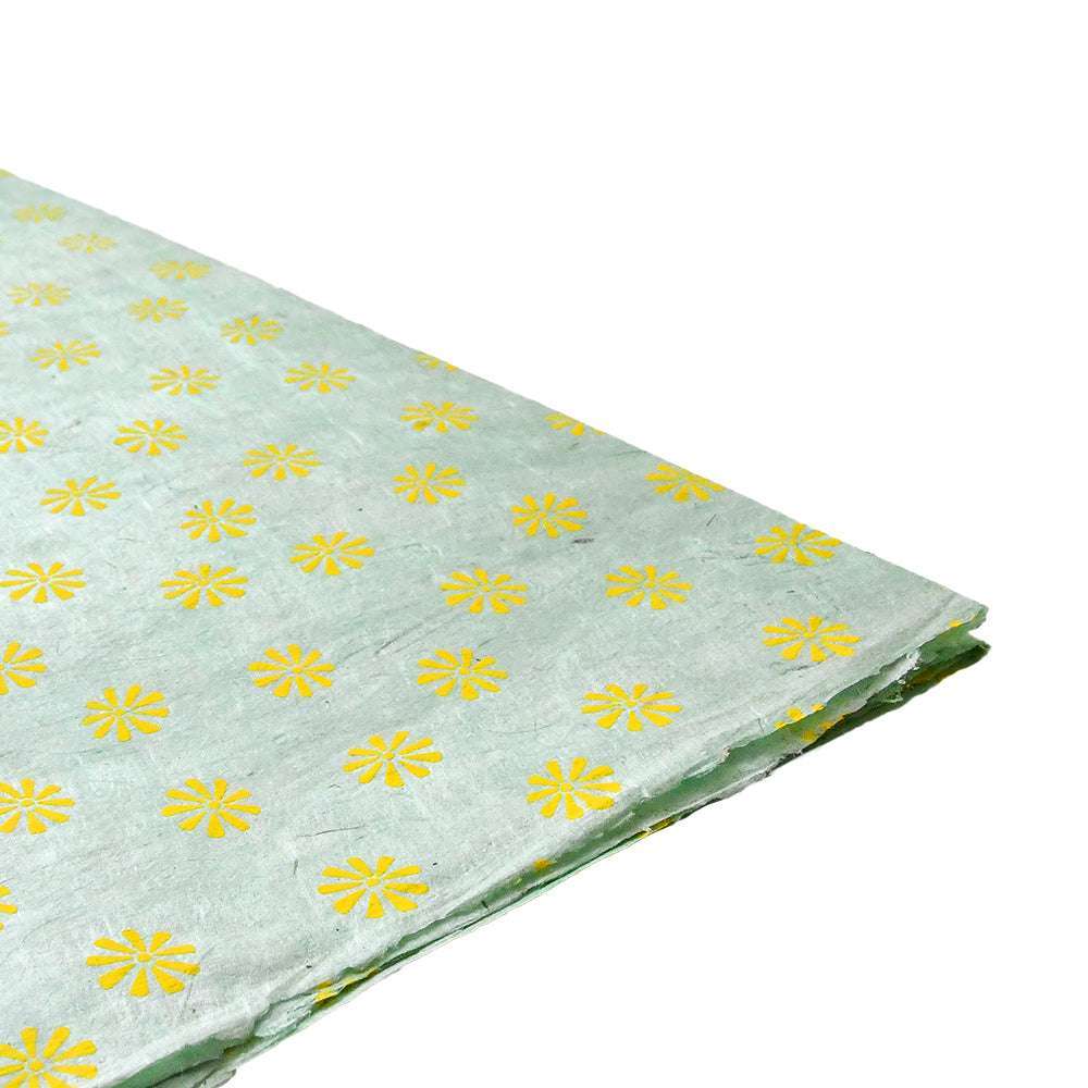 Hellgrünes Nepalpapier mit gelbem Blumenmuster, teilweise gefaltet - ideal als Geschenkpapier oder für Bastelprojekte. Marke: ☆.