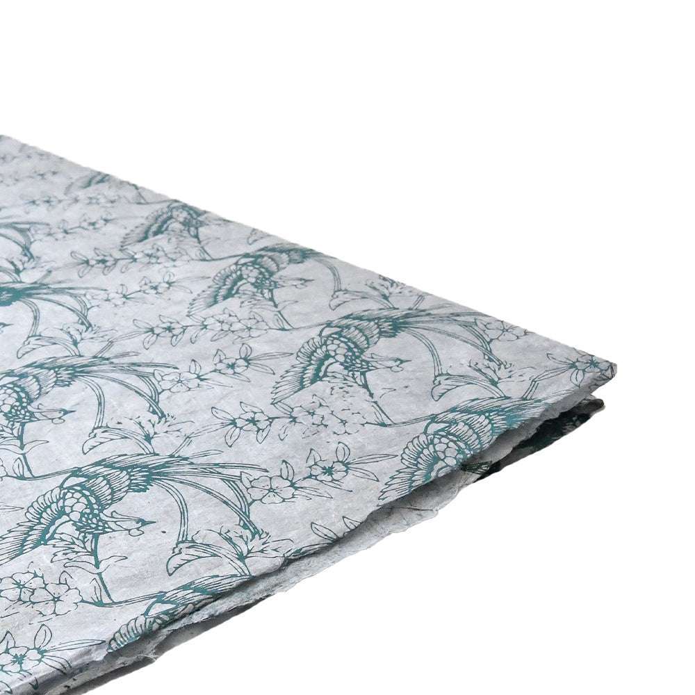 Ein Stapel ☆ Nepalpapier, handgeschöpft, mit einem tealfarbenen Vogel- und Zweigmotiv auf einem hellen, floral gemusterten Hintergrund.