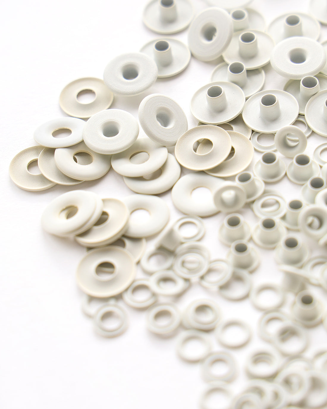 Eine Sammlung von verstreuten weißen Metallscheiben und -tüllen auf weißem Hintergrund.