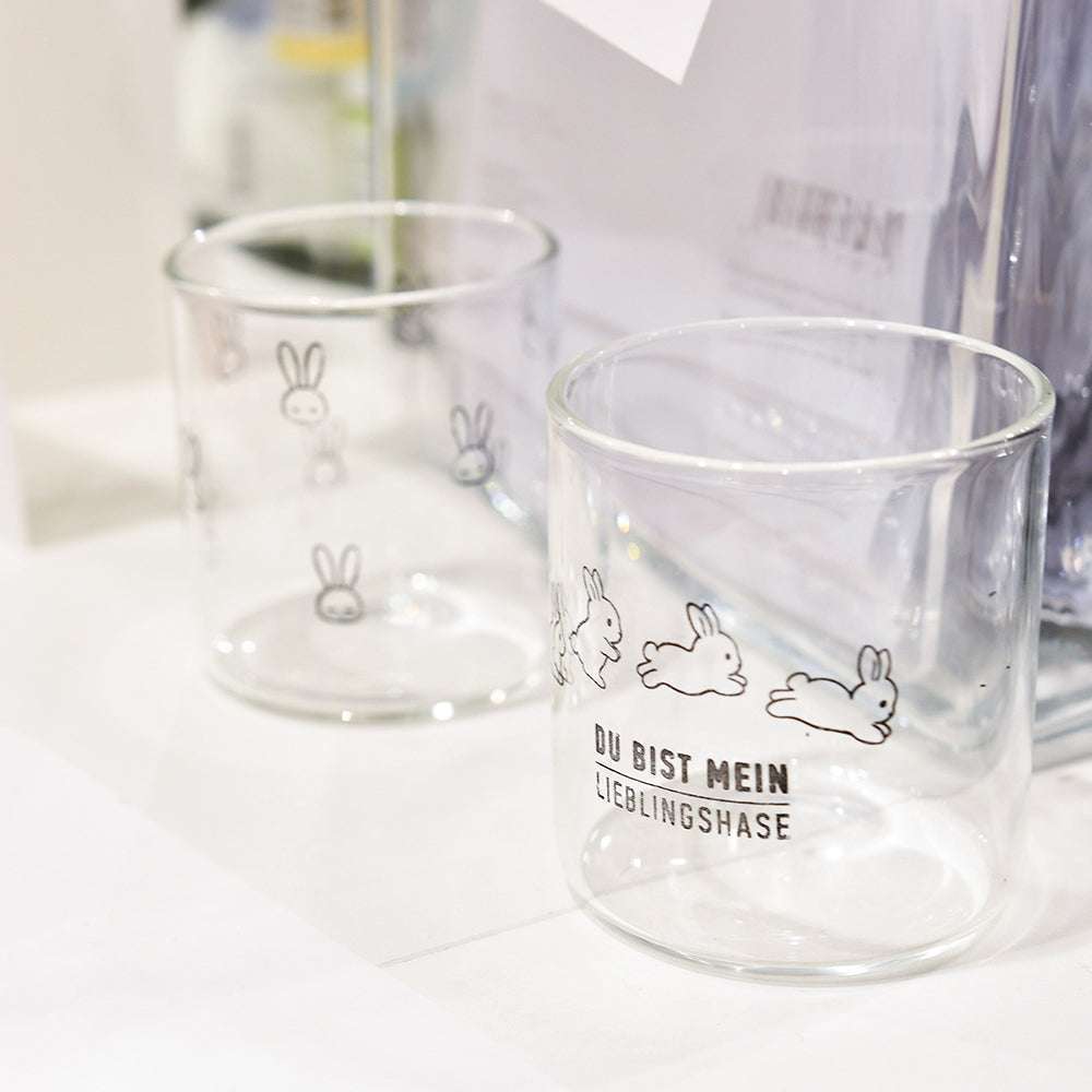 Zwei klare Alexandra Renke Gläser mit niedlichen weißen Hasenmotiven und deutschem "Osterspaß"-Text, platziert auf einer weißen Oberfläche - großartig für die Kombination mit Ihren Lieblings-Photopolymer-Klarsichtstempeln zu Ostern.