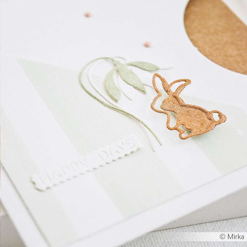 Eine Papierkarte mit einem kleinen braunen Hasen und einer grünen Pflanze, die mit dem Weidenkätzchen DieCut System von Alexandra Renke ausgestanzt wurden, vor einem klaren weißen Hintergrund.