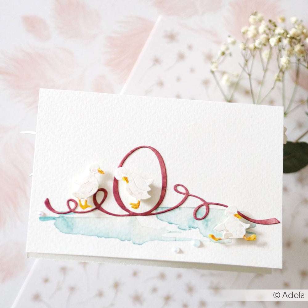 Handgefertigte Karte mit drei Enten, einem rosa Band mit der Aufschrift "Liebe" und zarten Trockenblumen, hergestellt mit Alexandra Renke Stanzen für Designpapier für präzise Formen und elegante Details.