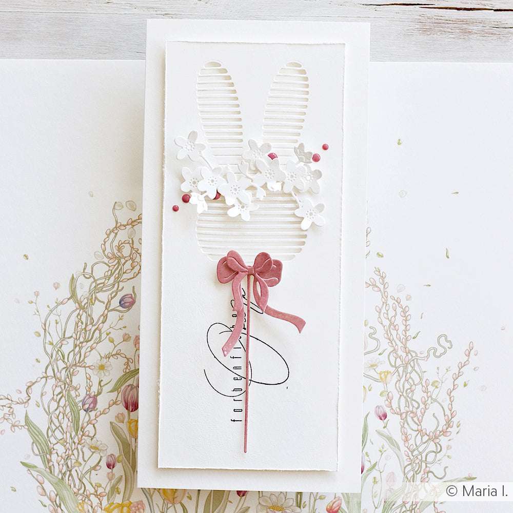 Handgemachte Karte mit Hasenohren, weißen Blumen, rosa Punkten und einer rosa Schleife auf weißem Blumenhintergrund, hergestellt mit der Motivstanze Lamellen Hasenkopf von Alexandra Renke.