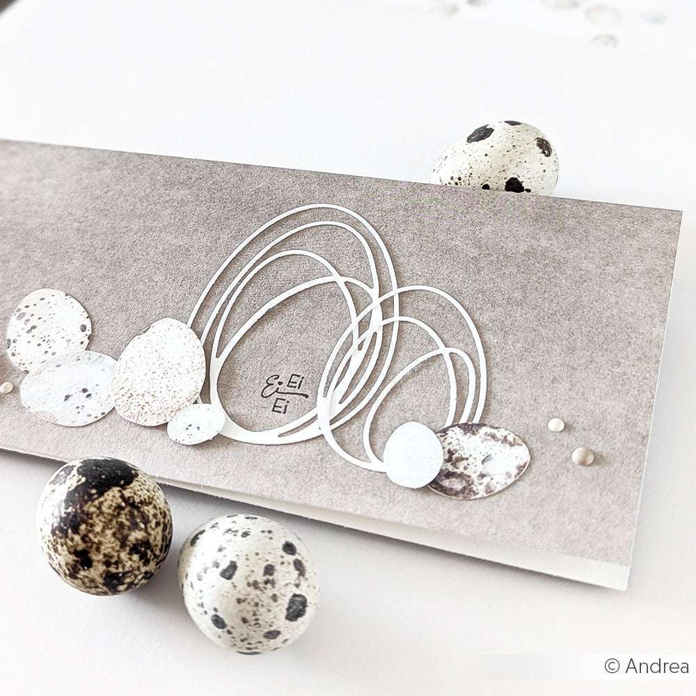 Eine Karte mit abstrakten Eimotiven, die mit der Alexandra Renke Motivstanze Outline Ei klein gestaltet wurden, wird neben drei gesprenkelten Eiern auf einer weißen Fläche präsentiert.