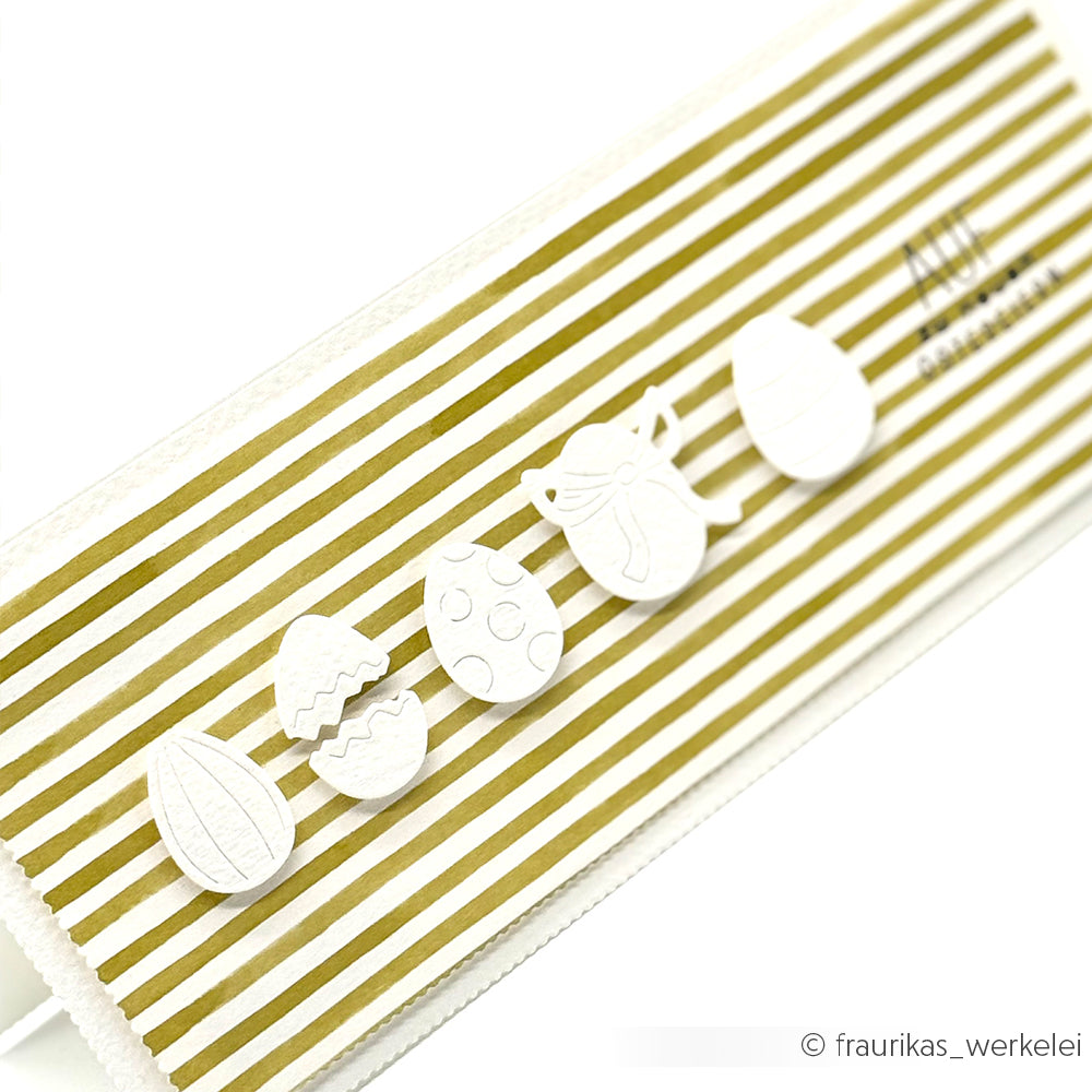 Weiße Ostereier, die mit einer Alexandra Renke-Stanze ausgestanzt wurden, verleihen dieser goldenen, schräg gestreiften Karte Charme.