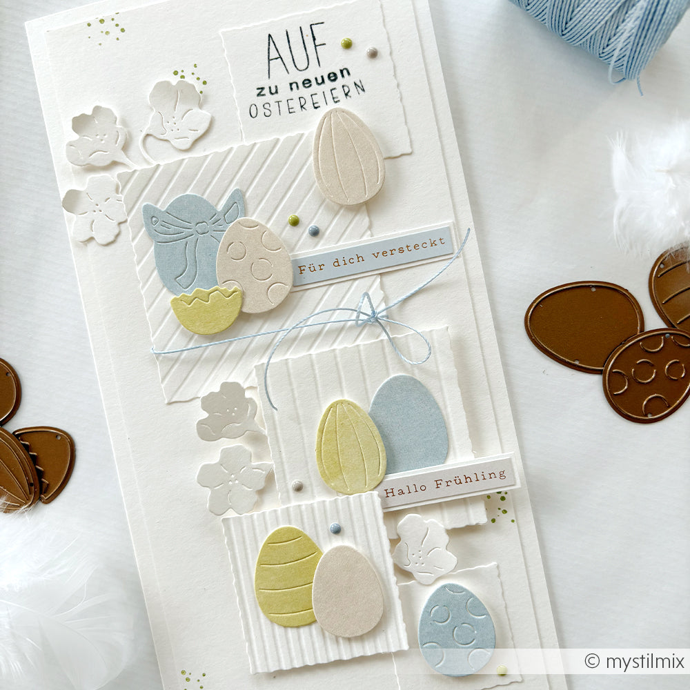 Handgefertigte Osterkarte von Alexandra Renke mit pastellfarbenen Eiern, Blumen und deutschem Text auf weißem Untergrund, hergestellt mit Motivstanze Eier-Set für einzigartige Details.