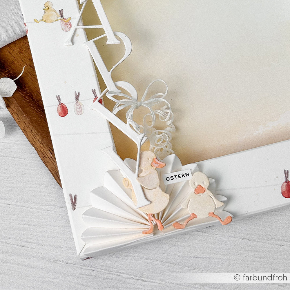 Weißer Bilderrahmen mit Papierenten, Ostereiern und Fächerdekorationen, gefertigt mit Alexandra Renke Stanzsysteme auf einer hellen Holzoberfläche - perfekt für Oster Garten-Spaß.