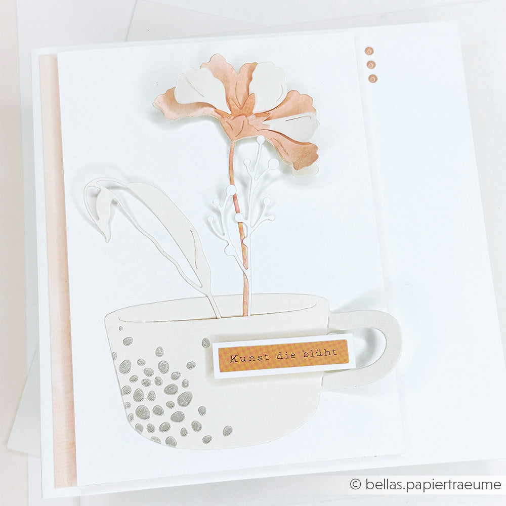 Eine handgefertigte Karte von Alexandra Renke mit einem Tassen- und Blumenmotiv, hergestellt mit Designpapieren und DieCut Systemen, verziert mit dem deutschen Text "Kunst die blüht.