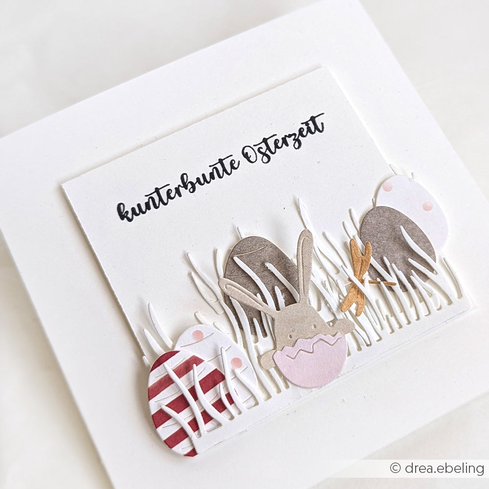 Handgemachte Osterkarte von Alexandra Renke mit Eiern, einem Hasen und Gras mit dem Text "kunterbunte Osterzeit" - hergestellt mit DieCut Systemen und Motivstanze Neugierige Häschen für zusätzlichen Charme auf weißem Hintergrund.