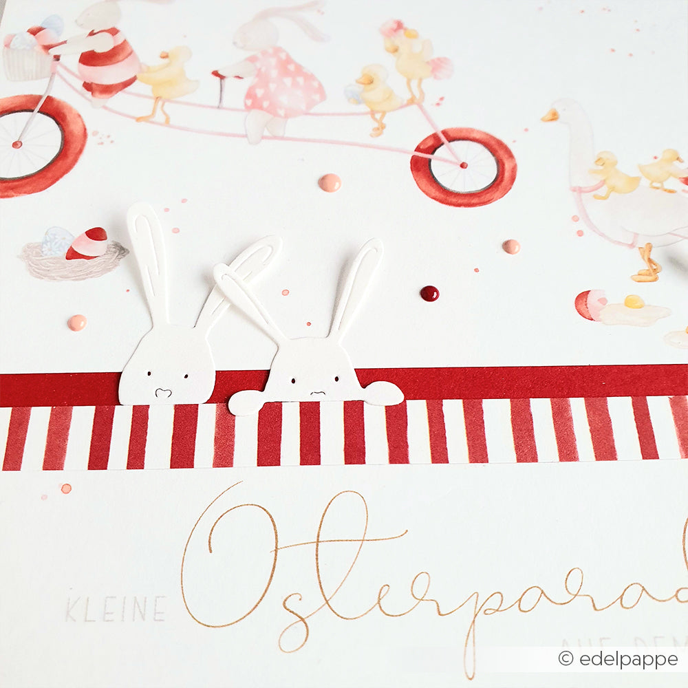Zwei weiße Cartoon-Hasen, inspiriert von Alexandra Renkes Motivstanze Neugierige Häschen Dies, lugen über einen rot gestreiften Rand mit einer skurrilen Fahrradszene im Hintergrund.