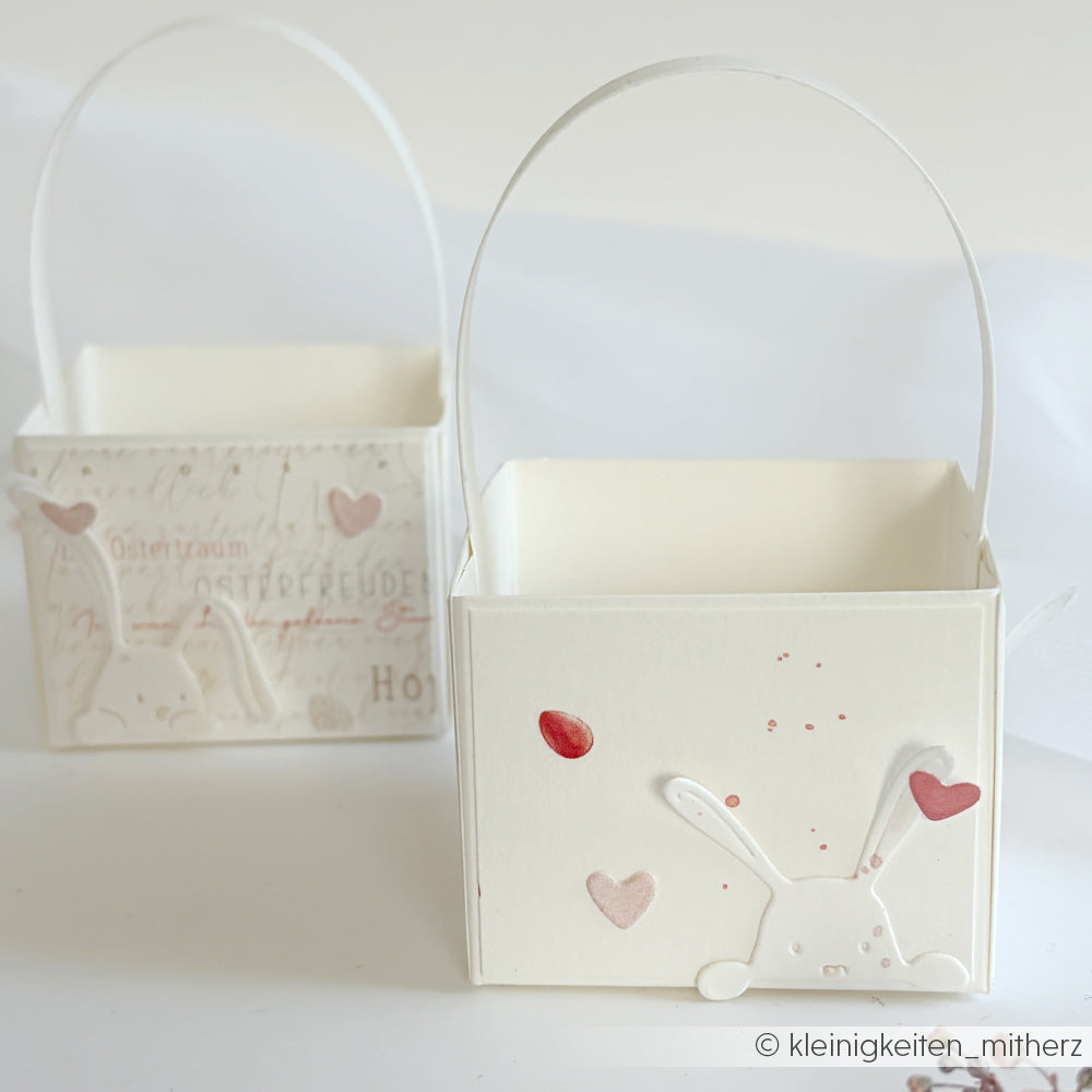 Zwei weiße Papierkörbe mit Hasengesichtern, Herzakzenten und Henkeln von Alexandra Renke, hergestellt mit Designpapieren und Stanzsystemen, auf weißem Hintergrund.