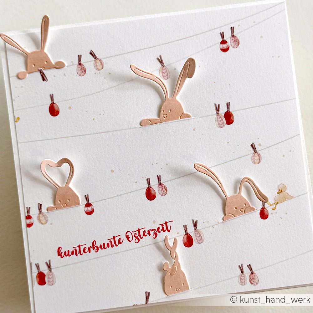 Handgemachte Osterkarte mit niedlichen Hasen-Illustrationen aus der Alexandra Renke Motivstanze Neugierige Häschen und bunten Eiern auf Linien, Text "kunterbunte Osterzeit". Ideal für Fans von Stanzsystemen und bunten Designpapieren.