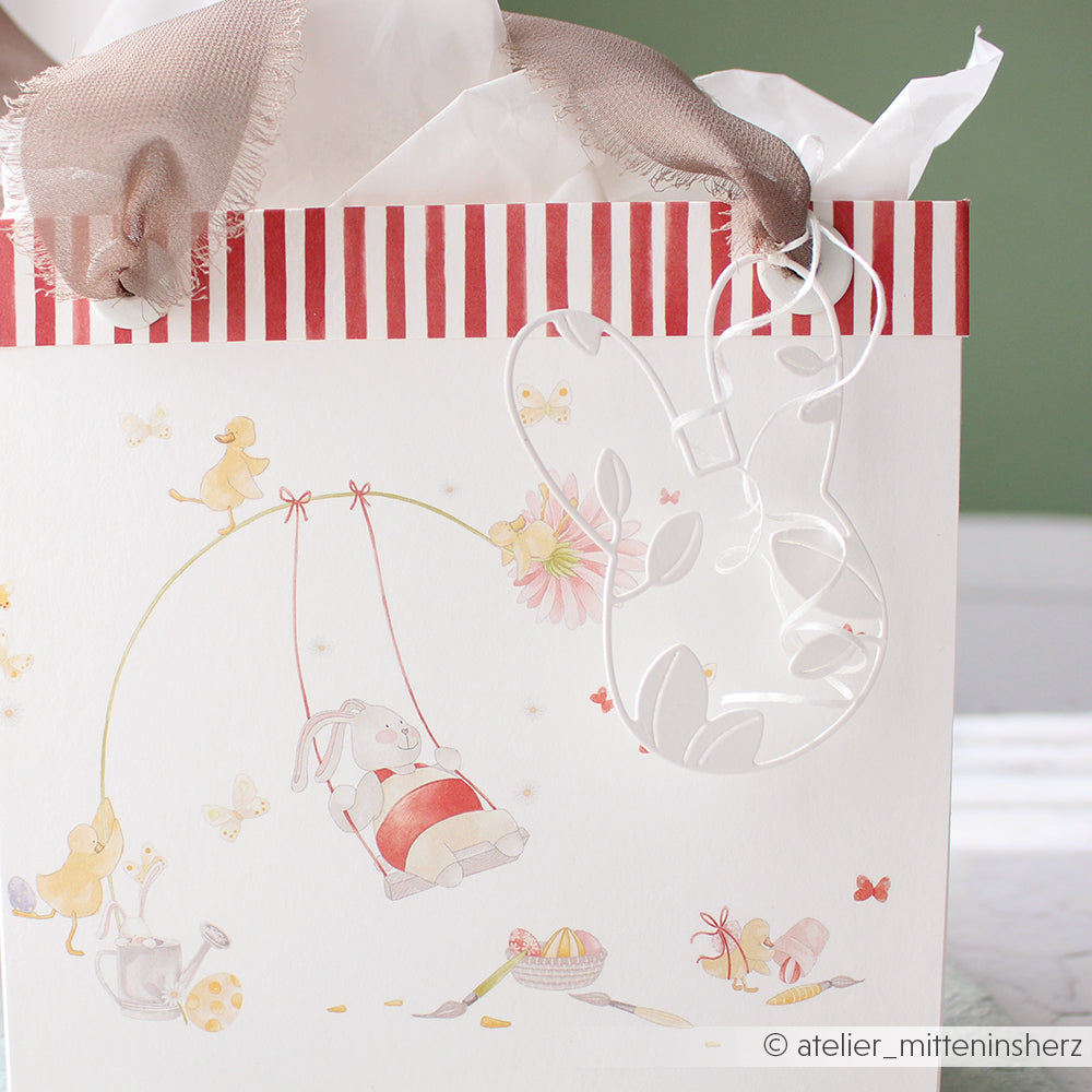 Alexandra Renke Geschenktüte mit roten Streifen, Hasenmotiv und transparentem Ornament in Hasenform aus der Motivstanze Hasenkopf. Inklusive Seidenpapier im Inneren für eine besondere Note.