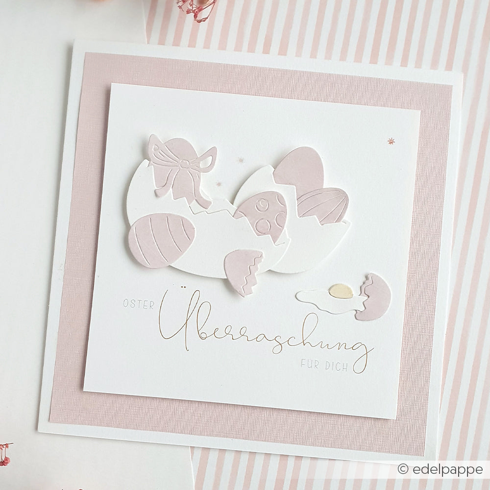 Eine pastellfarbene Osterkarte von Alexandra Renke mit zerbrochenen Eierschalen, verzierten Eiern und dem Text "Oster Überraschung für dich", hergestellt mit Motivstanze Eierhälften und DieCut Systemen für filigrane Details.