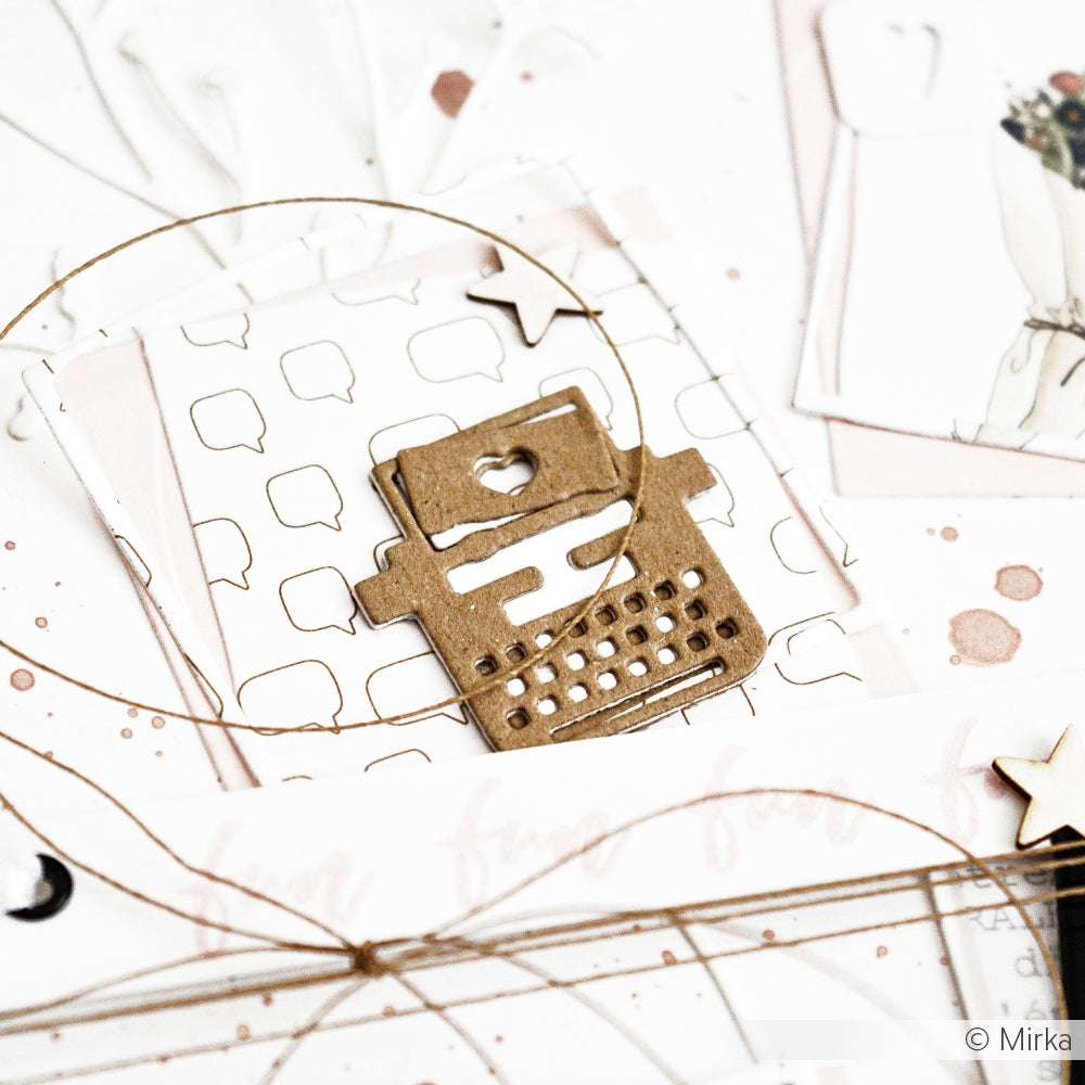 Ein Pappausschnitt einer Schreibmaschine von Alexandra Renke liegt auf Designpapier, umgeben von Bindfäden, Sterndekorationen und Sprechblasen Gold Outline-Akzenten.