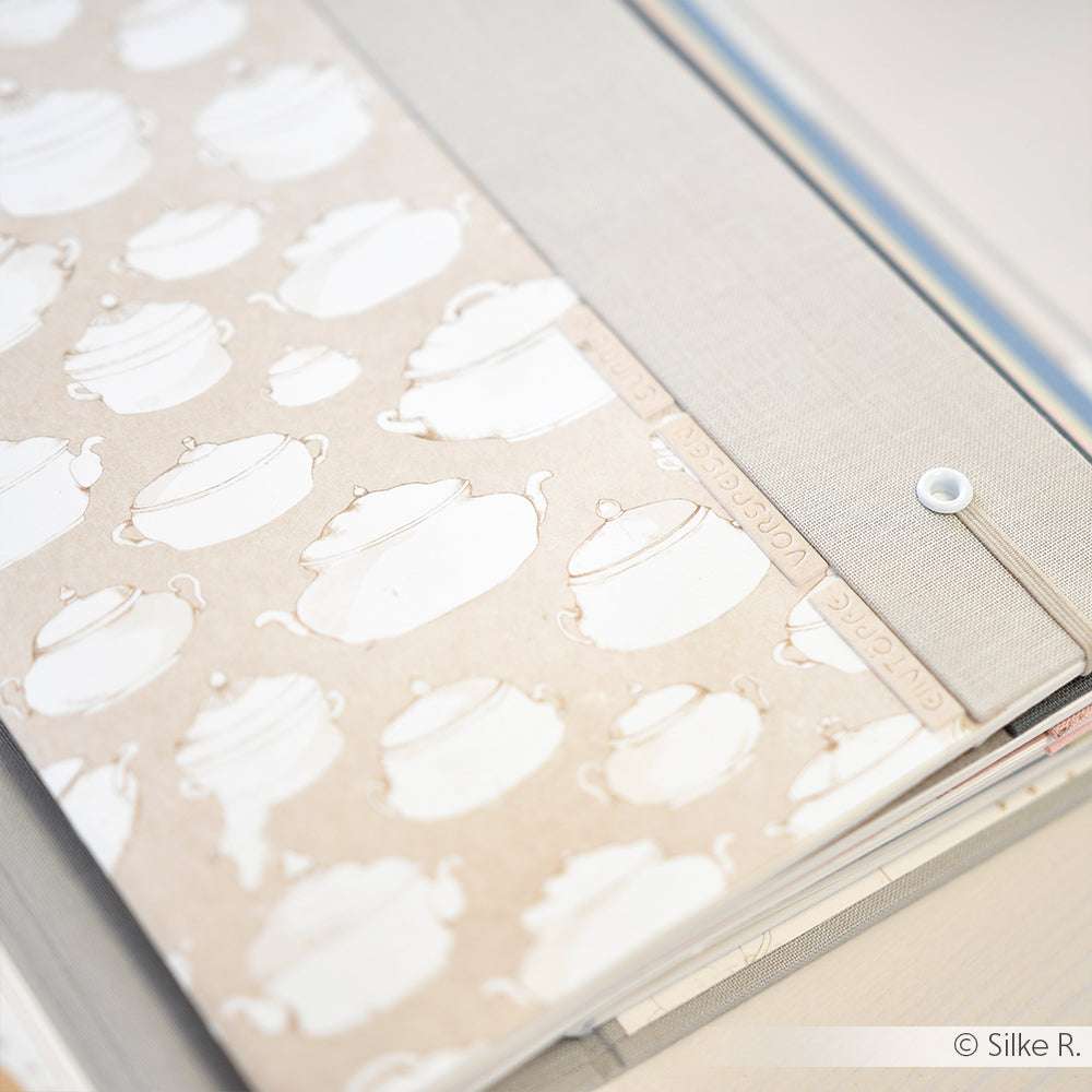 Scrapbook von Alexandra Renke mit Designpapier mit weißen Teekannen-Illustrationen und beschrifteten Trennblättern in einer sanften, neutralen Farbgebung - ideal für Liebhaber von Papierprojekten und Buchbinderei.