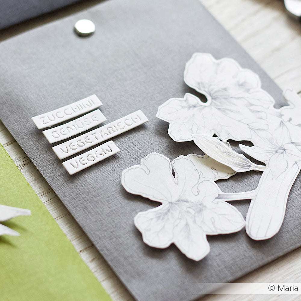 Graue Mappe mit ausgeschnittenen Blumen aus Alexandra Renke Designpapier und Mini-Etiketten "Zucchini, Gemüse, Vegetarisch, Vegan" - eine charmante Idee für Papierprojekte oder handgemachte Grußkarten.
