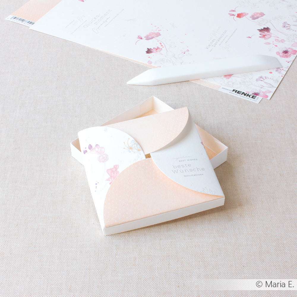 Eine Blumengrußkarte von Alexandra Renke aus Designpapier mit pfirsichfarbenem Umschlag liegt auf einer beigen Fläche neben Briefpapier und einem weißen Stift - perfekt, um Blumige Grüße zu versenden.