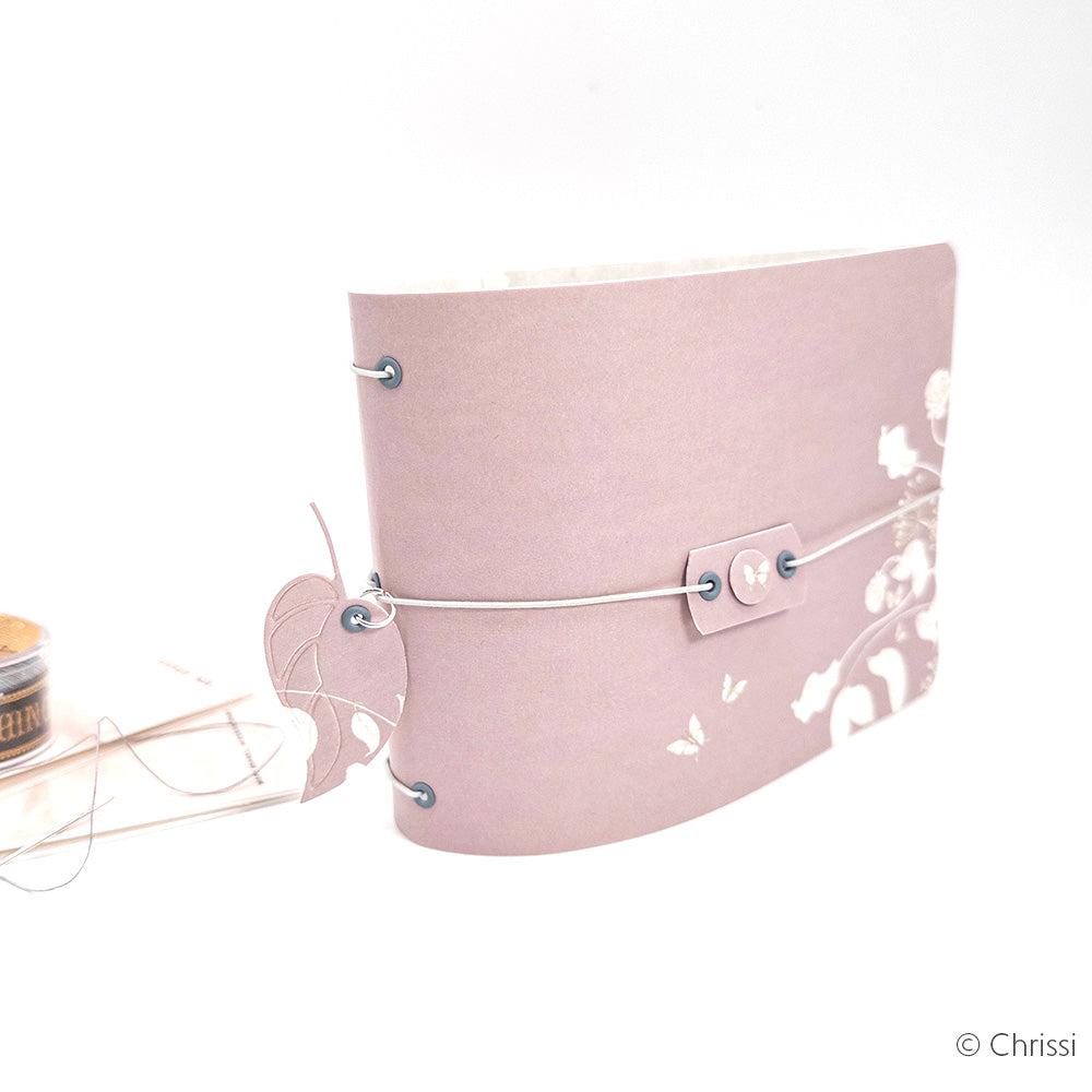 Dieses zartrosa geblümte Tagebuch von Alexandra Renke ist aus Designpapier gefertigt, hat einen Kordelverschluss, ein blattförmiges Etikett und ist mit zarten weißen Blumenmustern verziert.