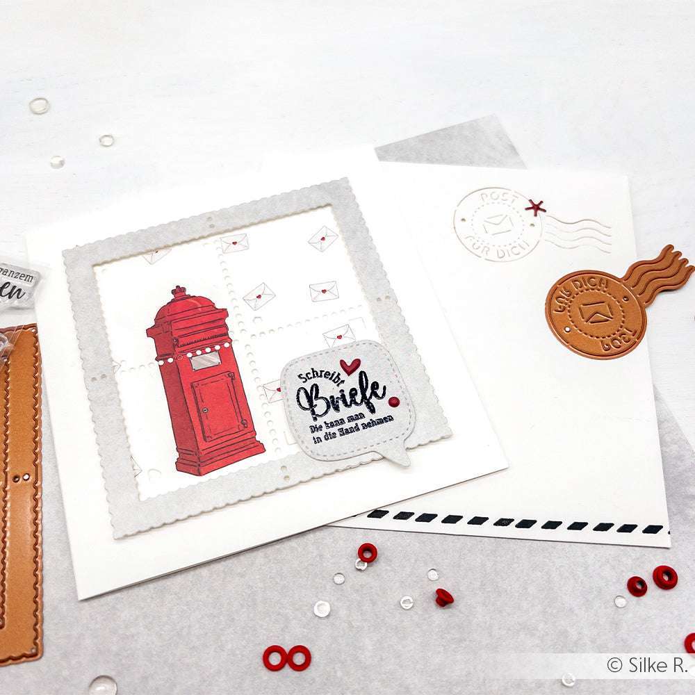 Handgefertigte Karte von Alexandra Renke mit rotem Briefkasten, Mini-Umschlägen und deutschem Text auf Designpapier, mit einem weißen Umschlag, der mit Briefmarken verziert ist.