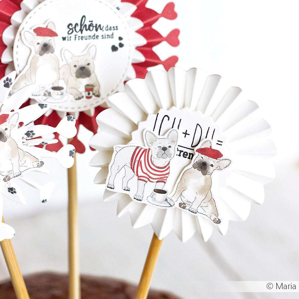 Die Designpapier-Rosetten von Alexandra Renke zeigen niedliche französische Bulldoggen und deutsche Freundschaftsbotschaften auf Holzstäben - ideal für einzigartige Papierprojekte oder als reizvolle Akzente auf Grußkarten.