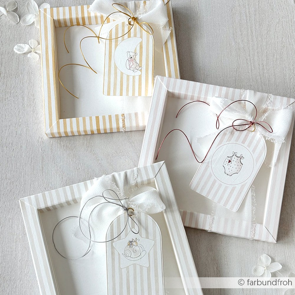 Drei pastellfarbene gestreifte Geschenkschachteln mit weißen Bändern und illustrierten Anhängern, gefertigt aus Alexandra Renke Designpapier, angeordnet auf einer hellen Fläche.